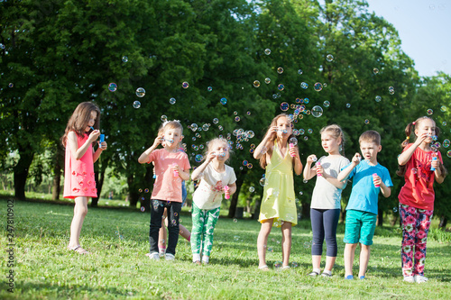Happy little kids blowing soap bubbles in summer park.