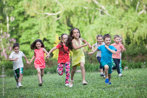 A group of happy children of boys and girls run in the Park on the grass on a Sunny summer day . The concept of ethnic friendship, peace, kindness, childhood. © Andrey