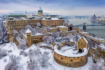 Budapest, Hungary - Aerial view of the snowy Buda Castle Royal Palace from above with the Szechenyi Chain Bridge and Parliament of Hungary at winter time