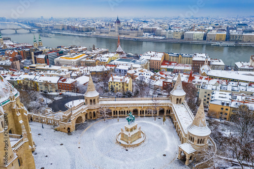 Budapest, Hungary - Aerial view of the snowy Fisherman's Bastion (Halaszbastya) at Buda district on a winter morning with Parliament of Hungary at background