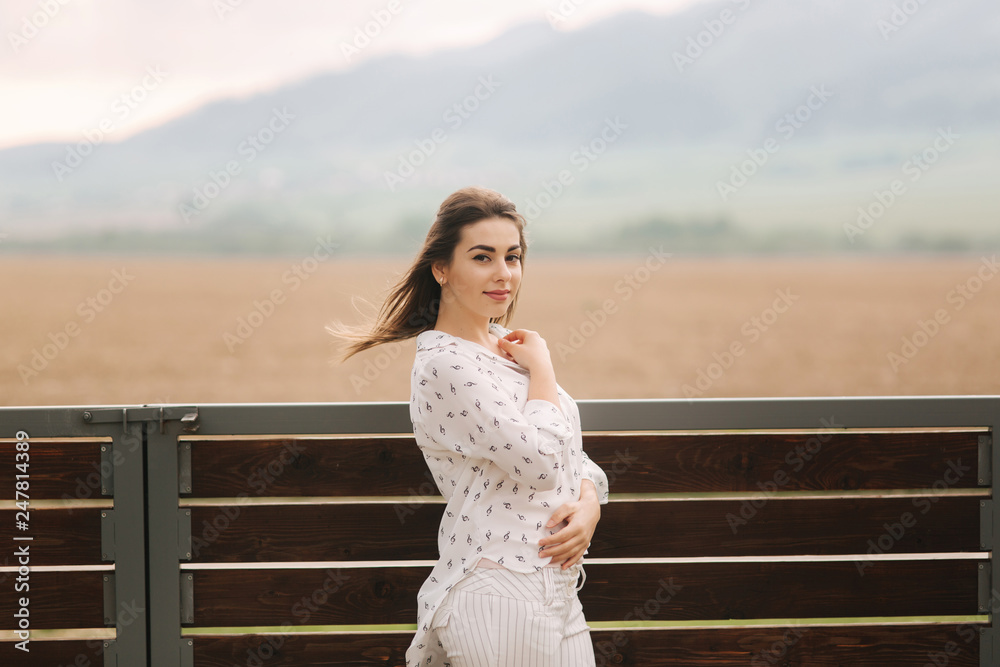 Obraz premium Attractive young girl stand outside in the village, Background of mountains. Bright photo. White clothes