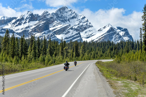 Riding On The Icefields Parkway - Two motorcyclists are enjoying the scenic ride on Icefields Parkway, with massive snow-covered Mount Patterson rising high in front of road, Banff National Park, AB.