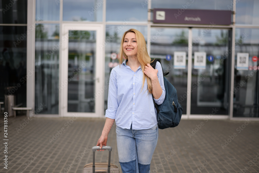 Young blonde hair business woman in shirt and denim pants standing near arrival terminal at the airport