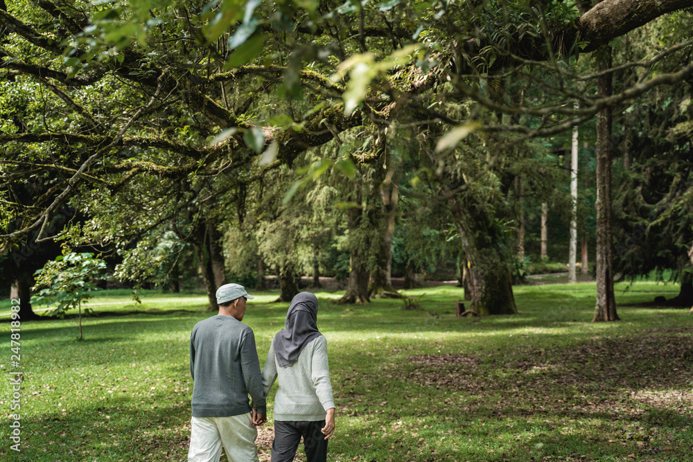 Fototapeta premium portrait of asian muslim senior couple walking in the garden together. shoot from behind