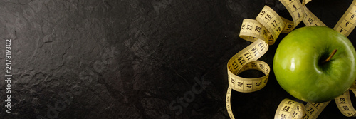 Green apple with measuring tape on wooden background. Apples and tape measure on a dark background. To lose weight and eat low-calorie apple to lose weight