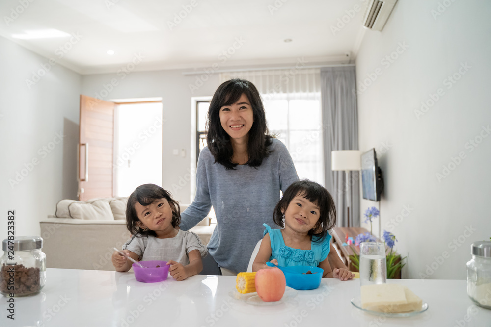 portrait of happy asian children having breakfast served by mom at home