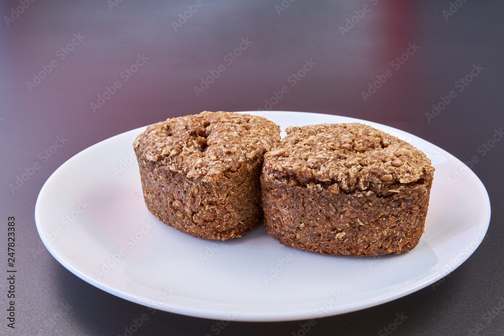 Vegan bread made at home with wheat germ and rye and buckwheat is lying on a white plate on a black background. healthy food. natural products Vegan bread made at home with wheat germ and rye and buckwheat is lying on a white plate on a black background. healthy food. natural products