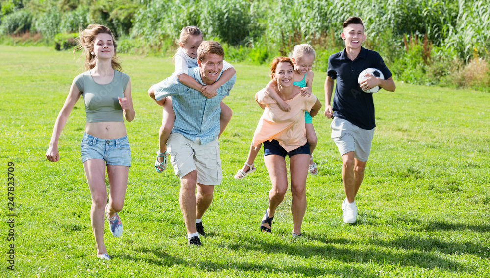 Fototapeta premium Smiling mother and father with four kids on green lawn