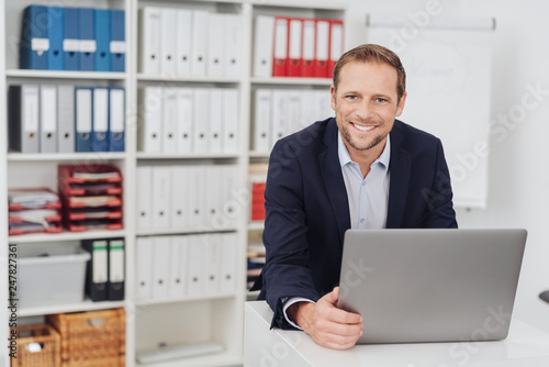 Smiling businessman sitting in office with laptop