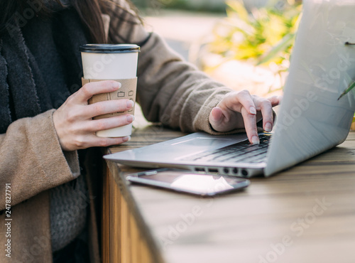 Young cute woman with laptop and coffee outdoor on wooden urban terrace