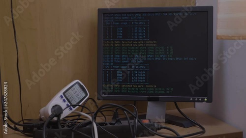 Power meter showing power consumption of ethereum cryptocurrency mining rig connected to computer with mining process displaying on monitor photo