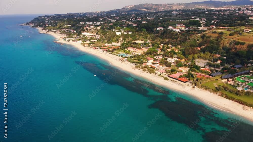 Two white pedalos float on turquoise sea along sandy beach with resorts. Aerial shot of Italian coastline Two white pedalos float on turquoise sea along sandy beach with resorts. Aerial shot of Italian coastline