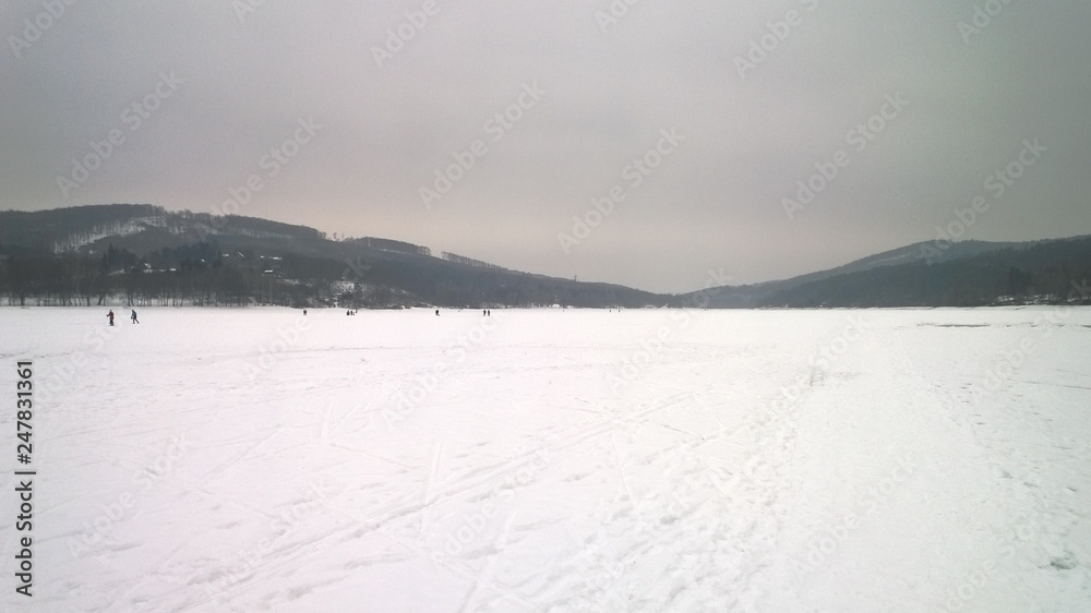 Photo of a large frozen lake covered in snow and surrounded by hills