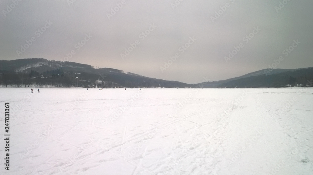 Photo of a large frozen lake covered in snow and surrounded by hills Photo of a large frozen lake covered in snow and surrounded by hills
