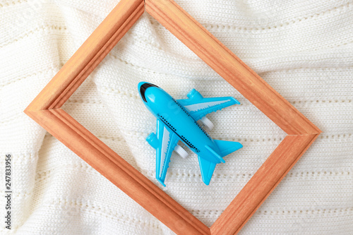 A blue toy plane in wooden frame on white knitted background, flat lay - trevelling and vacation concept
