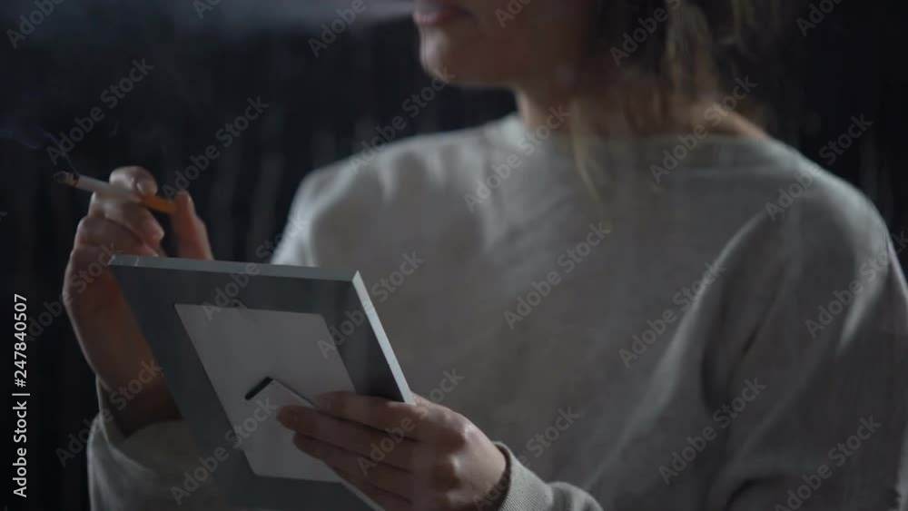 Woman with cigarette looking at photo in frame, remembering relatives, sadness Woman with cigarette looking at photo in frame, remembering relatives, sadness