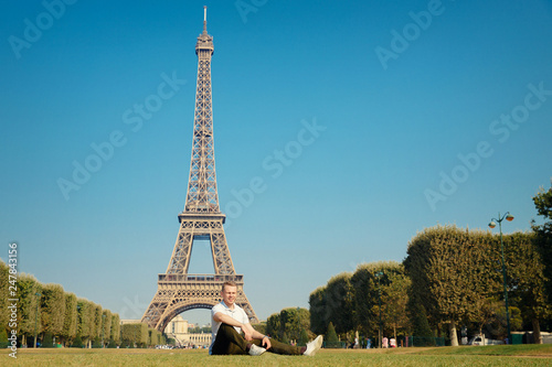 Eiffel Tower. Tourist guy sitting on lawn field, smiling