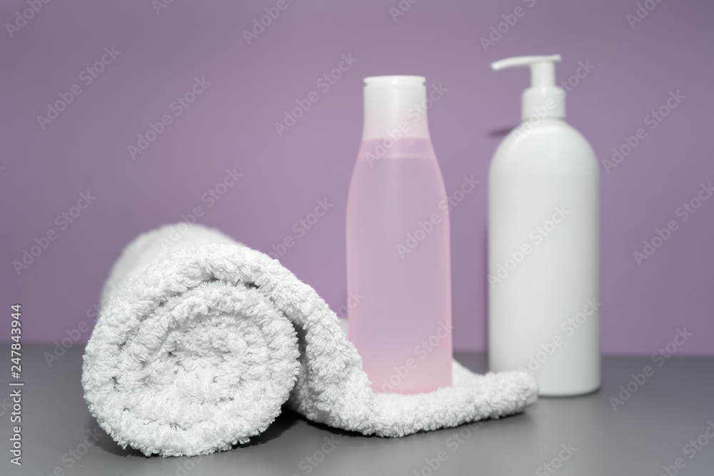 Cosmetic bottles with shampoo and towel in pink and white colors Cosmetic bottles with shampoo and towel in pink and white colors