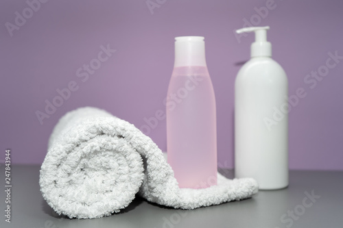 Cosmetic bottles with shampoo and towel in pink and white colors