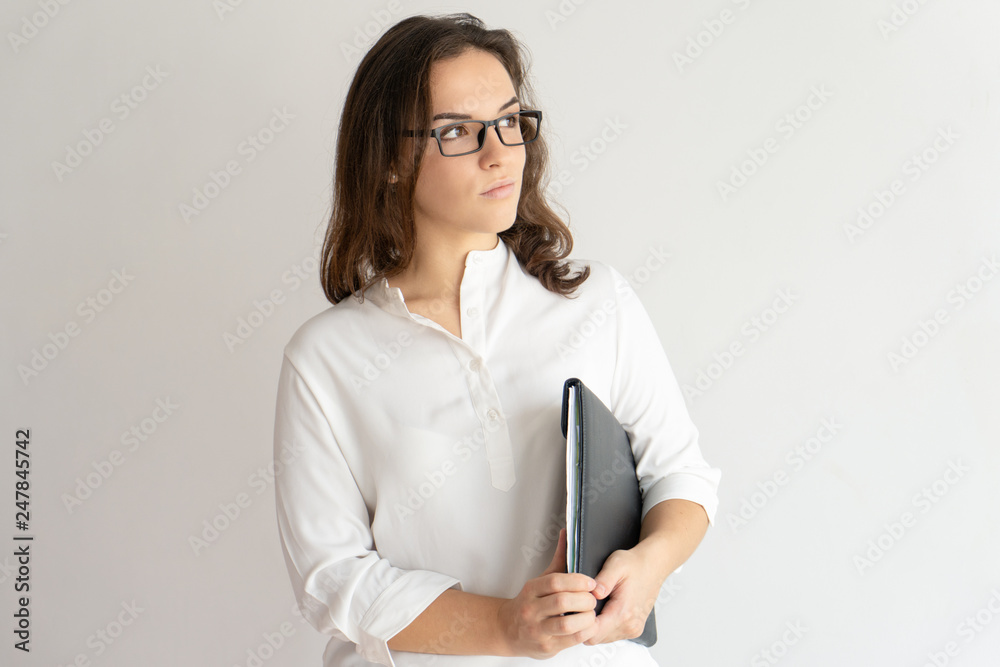 Pensive young woman holding file under her armpit Pensive young woman holding file under her armpit