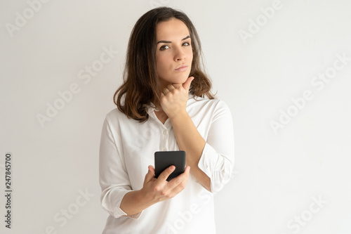 Pensive pretty young woman holding smartphone