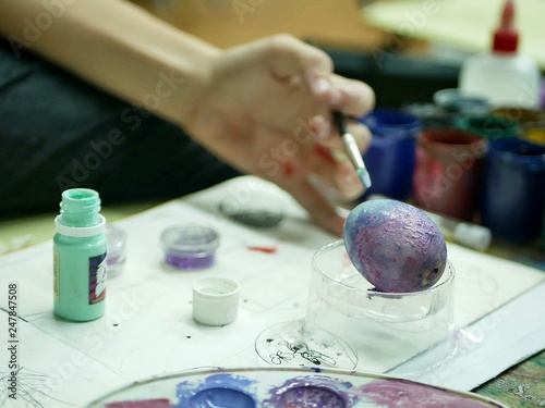 The hand of the student holds a brush with paint for coloring eggs for Easter, background art school workshop, preparation for the holiday of Easter