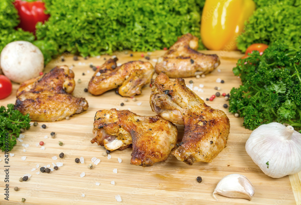 Fried chicken wings, baked chicken on a wooden board with cherry tomatoes, lettuce leaves, garlic, chilli pepper, rosemary, onion Fried chicken wings, baked chicken on a wooden board with cherry tomatoes, lettuce leaves, garlic, chilli pepper, rosemary, onion
