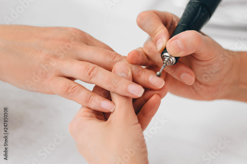 Beautician removing cuticle on female nails with special tool