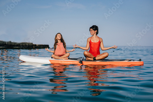 Mom and little daughter doing yoga on the paddle board © teksomolika