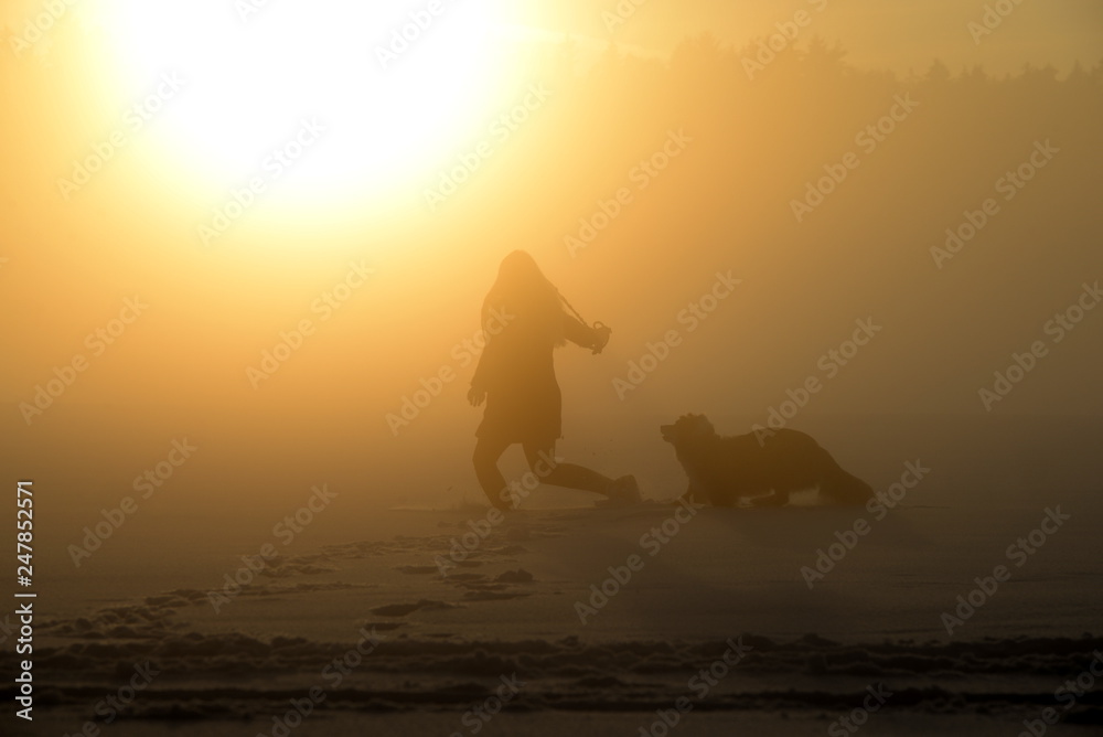 Abendspaziergang. Frau und Hund bei Nebel im Sonnenuntergang Abendspaziergang. Frau und Hund bei Nebel im Sonnenuntergang