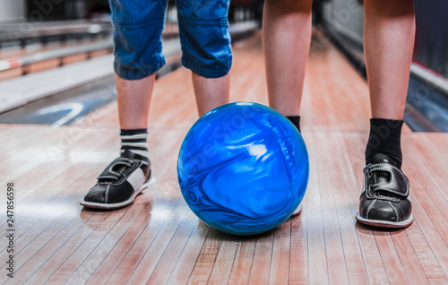 Photo of kids legs with blue bowling ball in a bowling alley. 