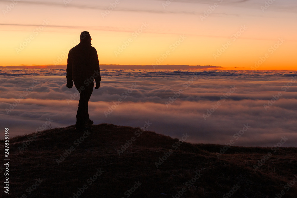 Uomo in silhouette al tramonto sopra un mare di nuvole