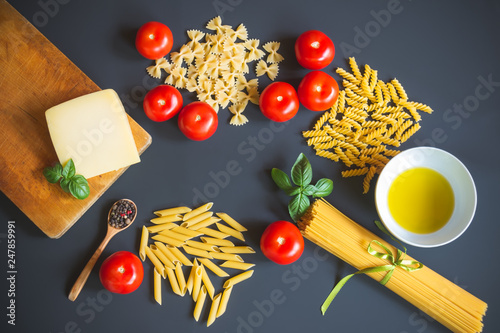 Different kinds of raw pasta and ingredients for cooking on dark background.