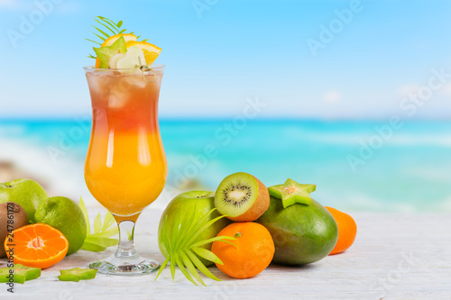 Summer cocktail with various tropical fruits around. Apple, kiwi, tangerine, orange, mango, carambola.