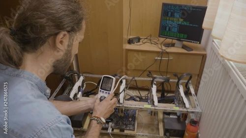 Young expert engineer examining with digital power meter cryptocurrency mining rig consumption photo