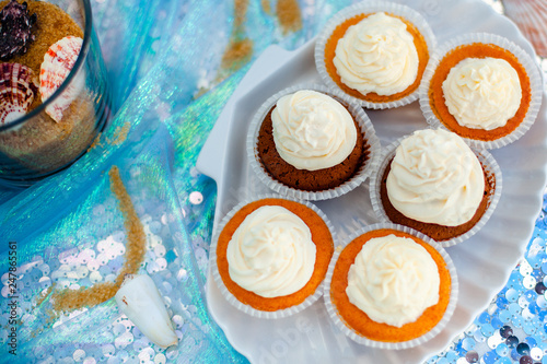 Vanilla cupcackes with white creamcheese on seashell shape plate. Silver fabric on the background photo