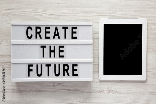 Modern board with text 'Create the future', tablet on a white wooden surface, top view. From above, flat lay, overhead.