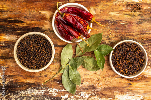 Fototapeta Naklejka Na Ścianę i Meble -  Set of spices - black pepper peas, clove, hot red pepper and bay leaf. On wooden bark, top view, close up.