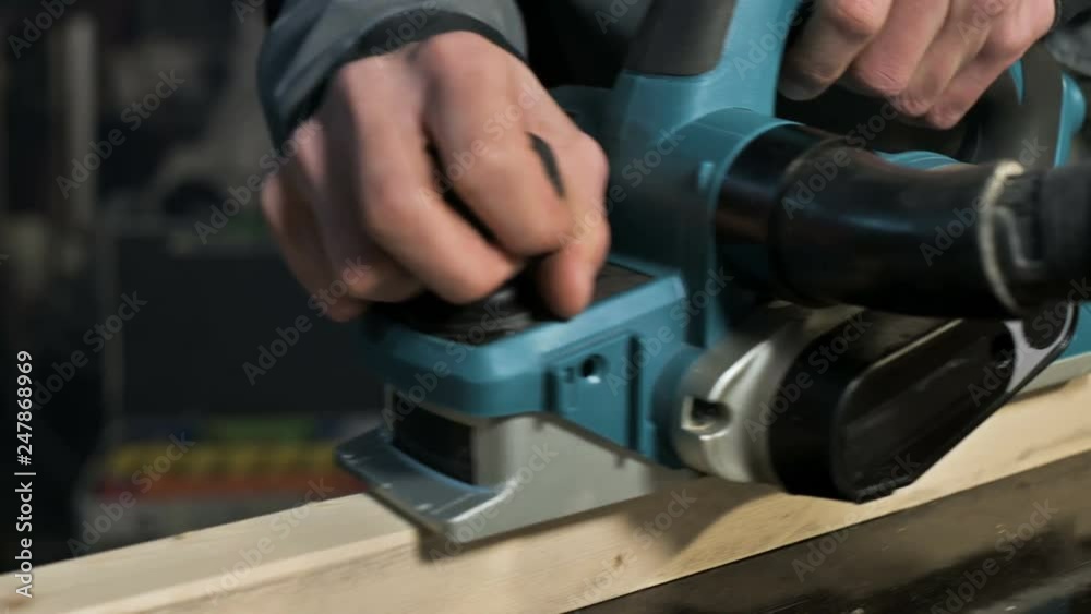 Close-up of a carpenter's hand working with an electric plane in a home workshop. Finishing wooden parts Close-up of a carpenter's hand working with an electric plane in a home workshop. Finishing wooden parts