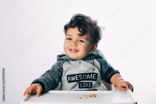 little 1 year old boy sitting with a very funny expression on his face, on a white background