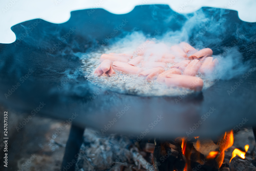Cooking sausages in a flat pan on the bonfire outdoor of winter.