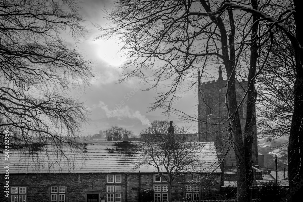 church tower or spire with roof tops of houses. snow with a winter sun. black and white. 