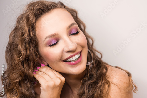 portrait beautiful young blonde curly girl posing in the studio with professional make-up and open tooth smile pink mood