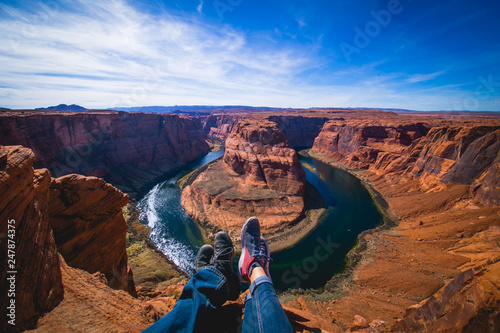 Men and woman sitting together in the edge of the canyon Horseshoe bend in Page, Arizona, United States. Male and female legs.