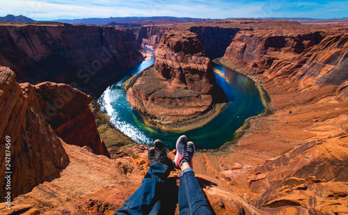 Men and woman sitting together in the edge of the canyon Horseshoe bend in Page, Arizona, United States. Male and female legs.
