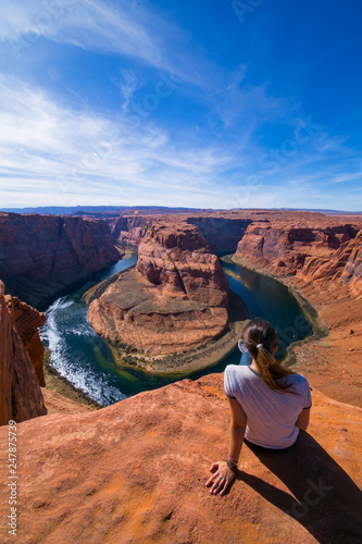 Young woman sitting in the edge of the Horseshoe Bend admiring the landscape. Page, Arizona, United States.