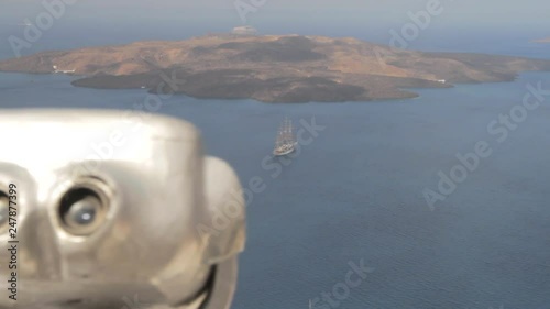 View of the Santorini Caldera, tracking past a pair of public binoculars. The volcanic island of Nea Kameni can be seen. photo