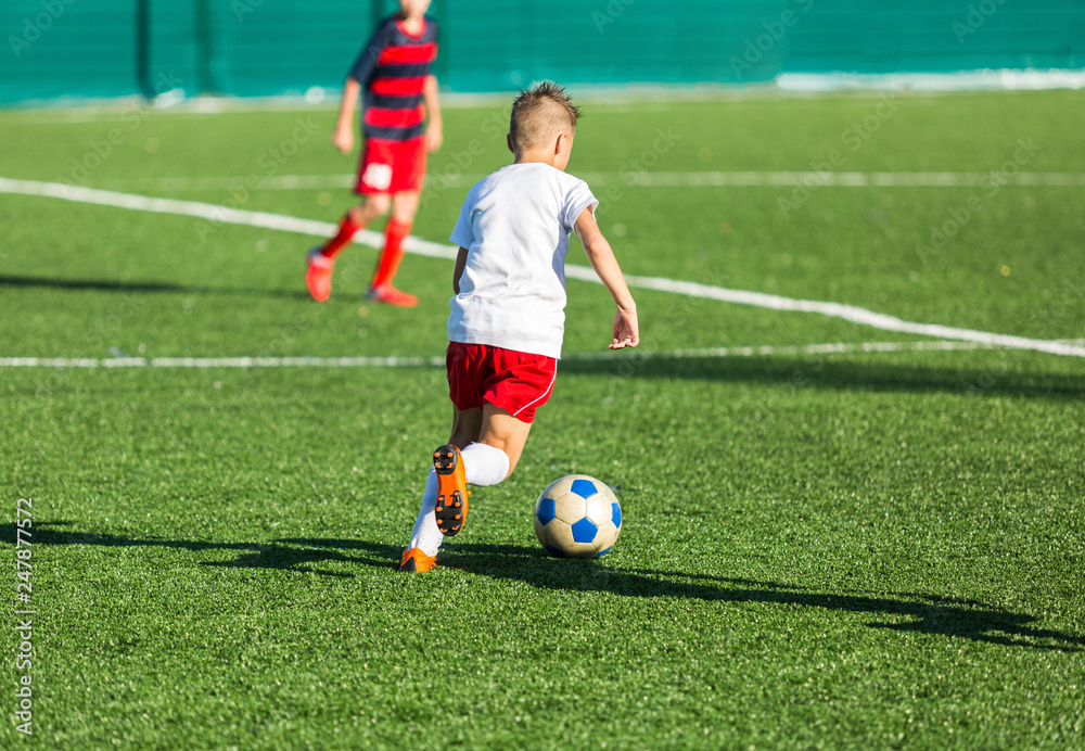 Boys in red white sportswear running on soccer field. Young footballers dribble and kick