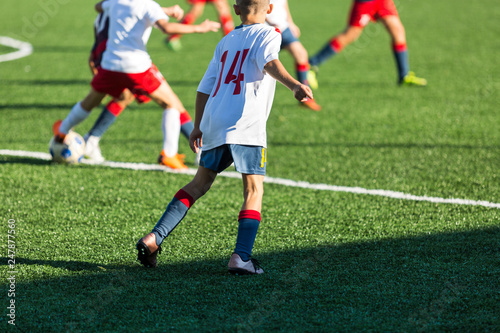 Boys in red white sportswear running on soccer field. Young footballers dribble and kick football ball in game. Training  active lifestyle  sport  children activity concept 