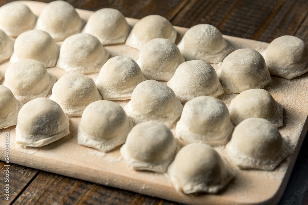 Uzbek national food Chuchvara, like dumplings, on a wooden board, in flour Uzbek national food Chuchvara, like dumplings, on a wooden board, in flour